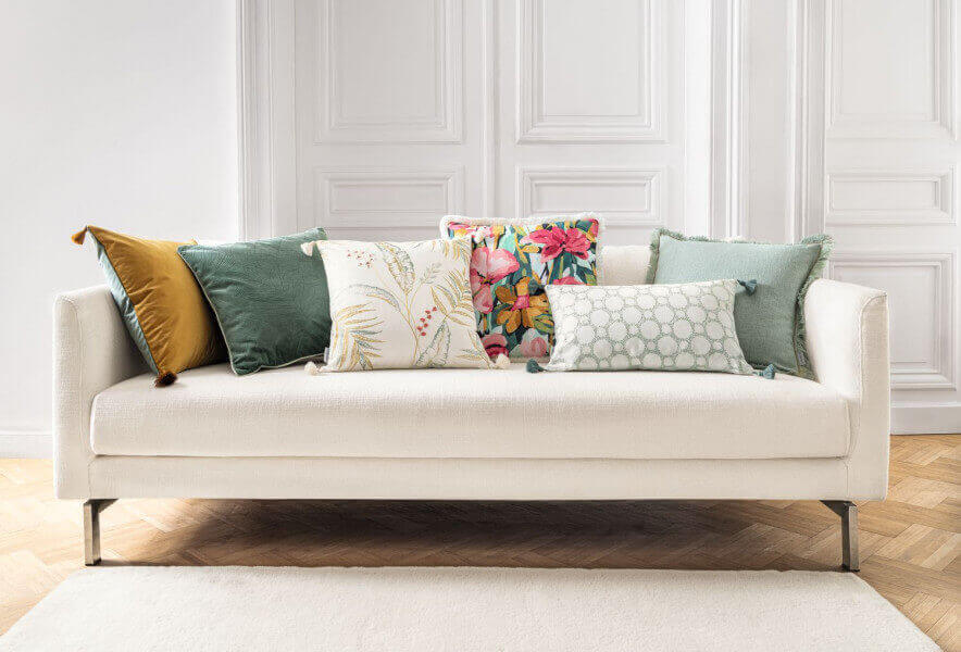 Funda de cojín Mison de Camengo 45x45 cm, diseño bordado con motivos botánicos en tonos verde, mostaza y rojo quisquilla, con borlas decorativas en las esquinas.